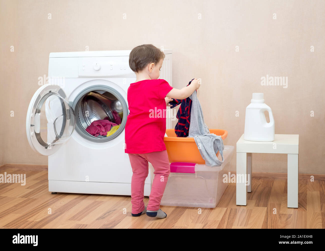 Little girl holding clothes near a washing machine Stock Photo