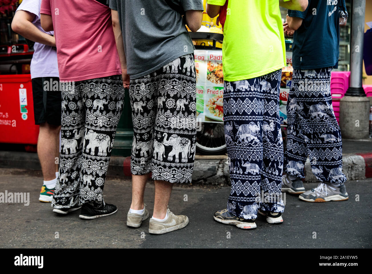 BANGKOK, THAILAND: Tourists wearing elephant-adorned trousers order food at  a stall on Khao San Road in Bangkok, Thailand on August 22nd, 2019.  Bangkok's bustling Khao San Road - a strip famous among