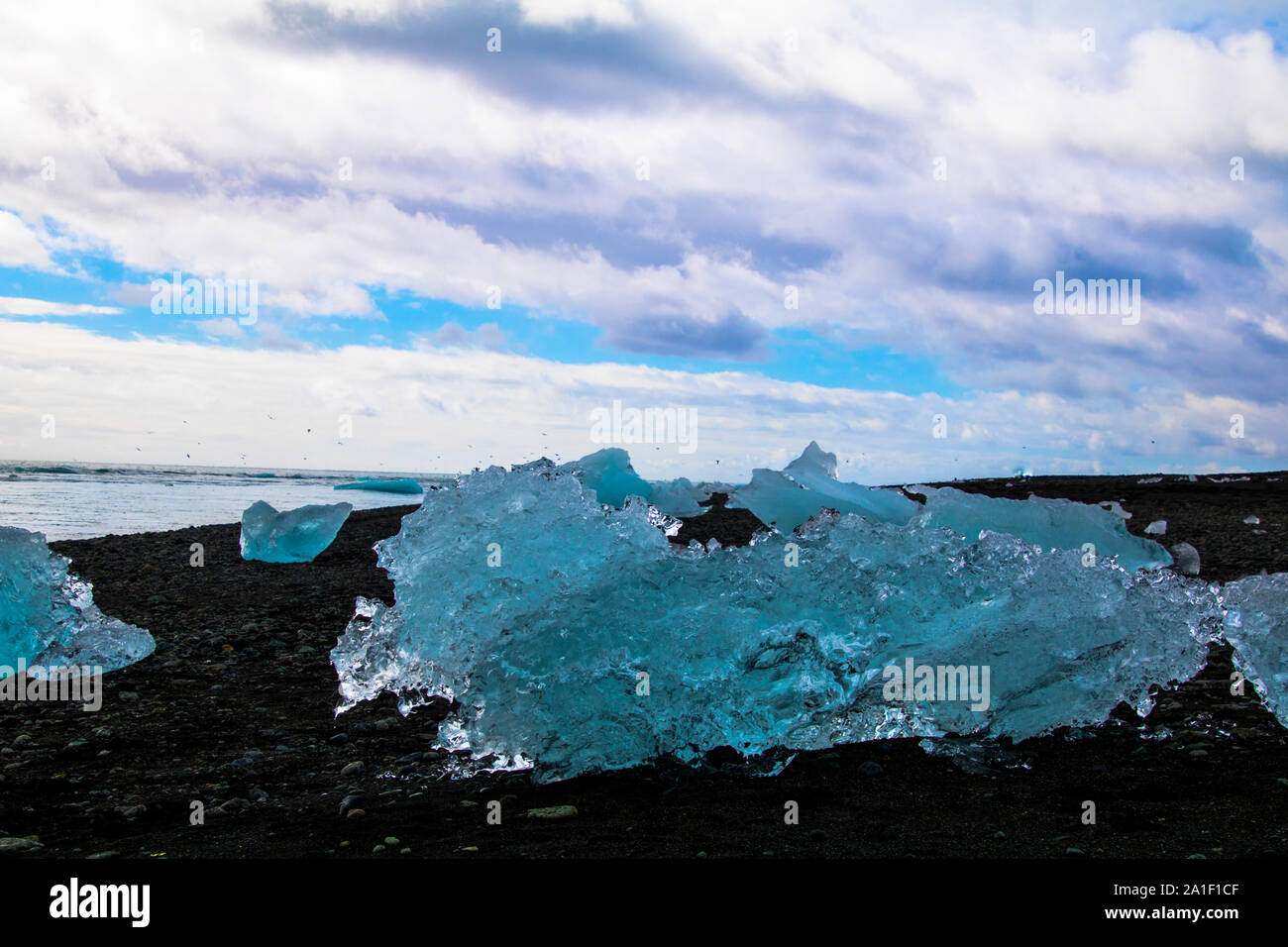 Ice floe on a black sand beach with sea and cloudy sky in the background. Photographed in the lagoon of Jökulsarlon in the south of Iceland Stock Photo