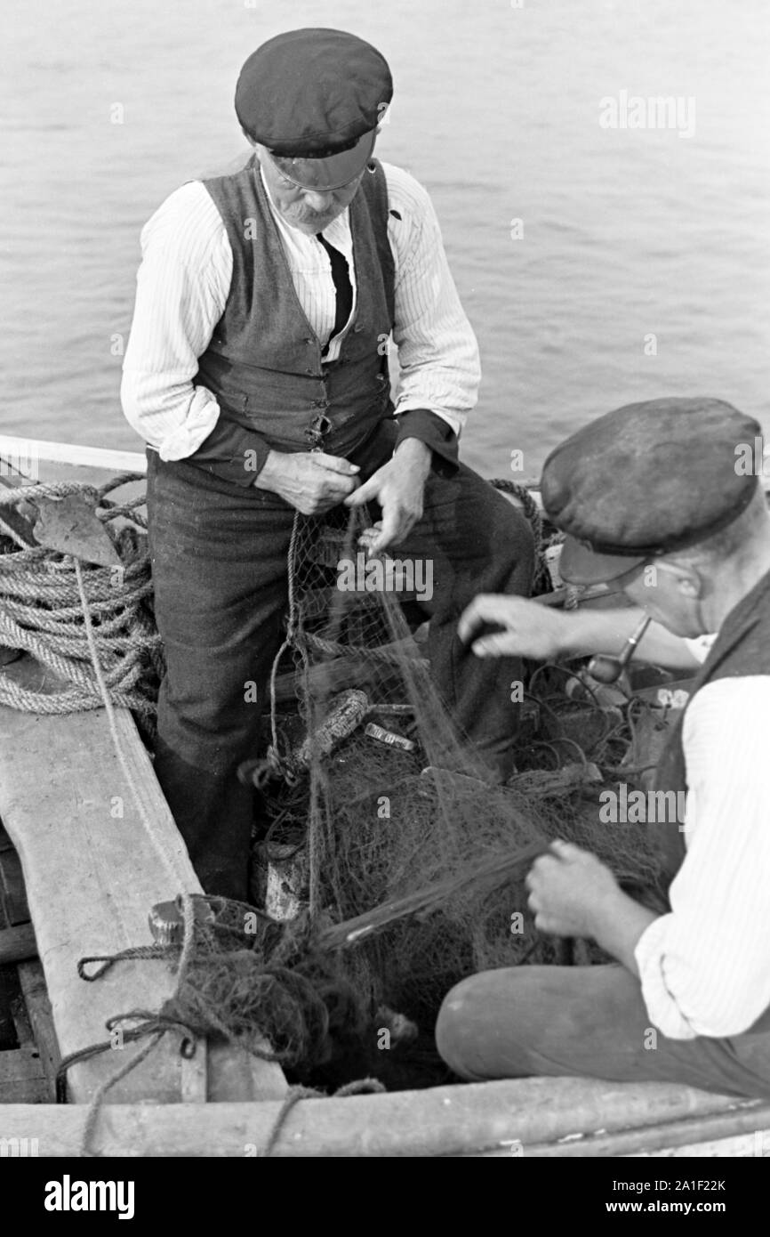 Fischer sortieren ihre Netze bevor sie sie zum Fischfang ins Meer auswerfen, Deutschland 1939. Fishermen assorting their nets before throwing them in the water, Germany 1939. Stock Photo