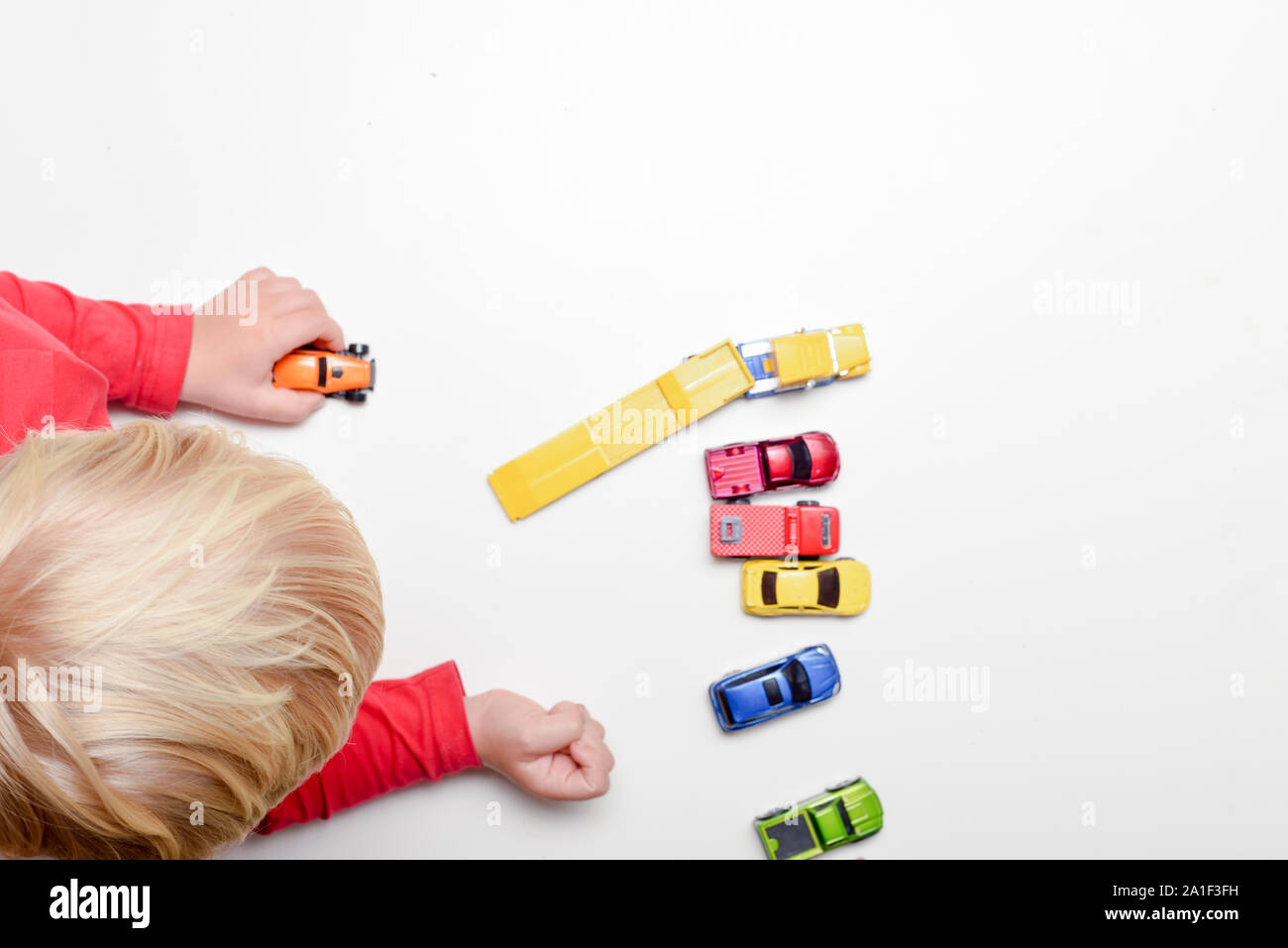 High angle shot of young blond child playing alone with toys Stock Photo