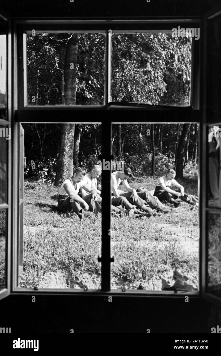 Männer sitzen in einer Pause im Gras, durch ein Fenster fotografiert, Deutschland 1939. Men having a break and sitting in a meadow, picture taken through a window, Germany 1939. Stock Photo