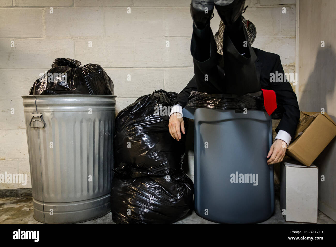 Businessman Sitting in Trash Can/Bin Next to Rubbish. Concept of Defeat and Despair. Dark Stock Photo. Stock Market Crash. Stock Photo