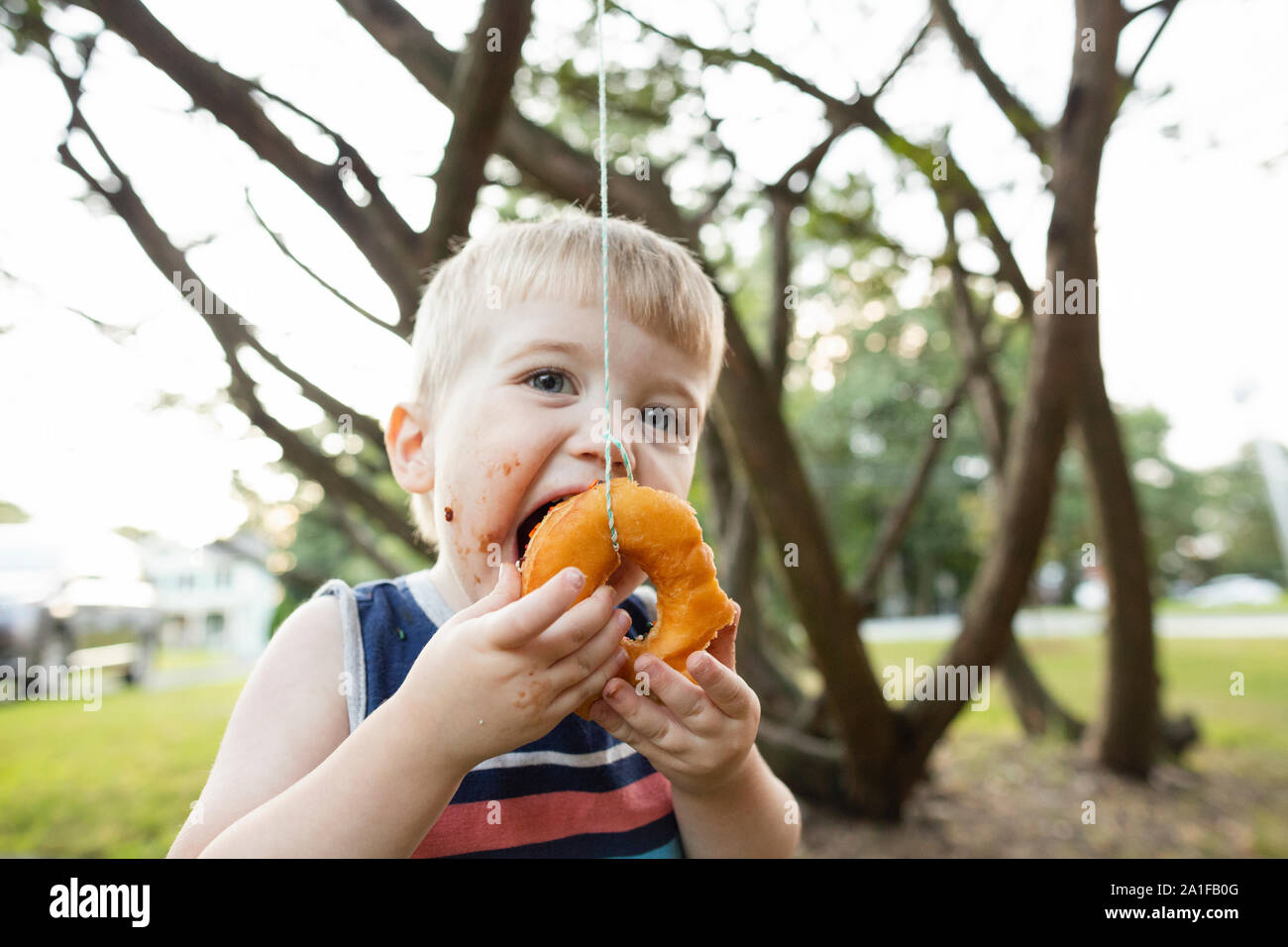 Happy playful toddler boy opens mouth to bite donut during party game Stock Photo