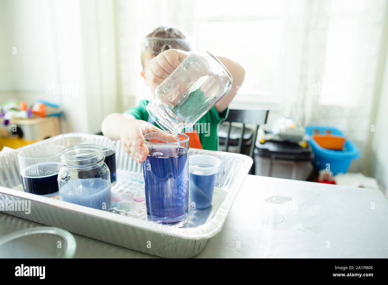 Anonymous child pours blue liquid into glass during science experiment Stock Photo