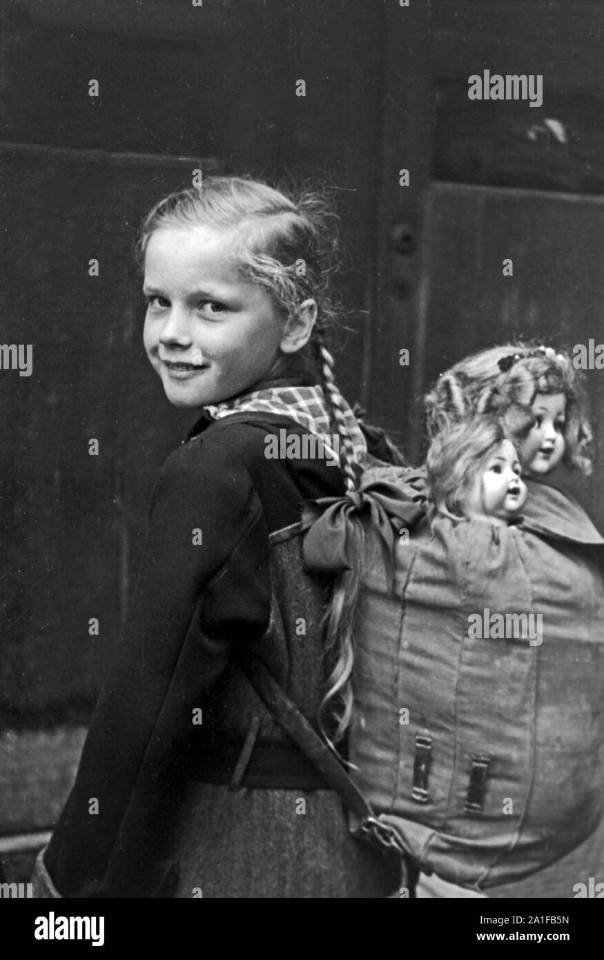 Mädchen mit ihrer Puppe im Gepäck auf dem Weg durch das verregnete Berlin, Deutschland 1949. Little girl with her dolls in a backpack on her way throuhgh the rainy Berlin, Germany 1949. Stock Photo