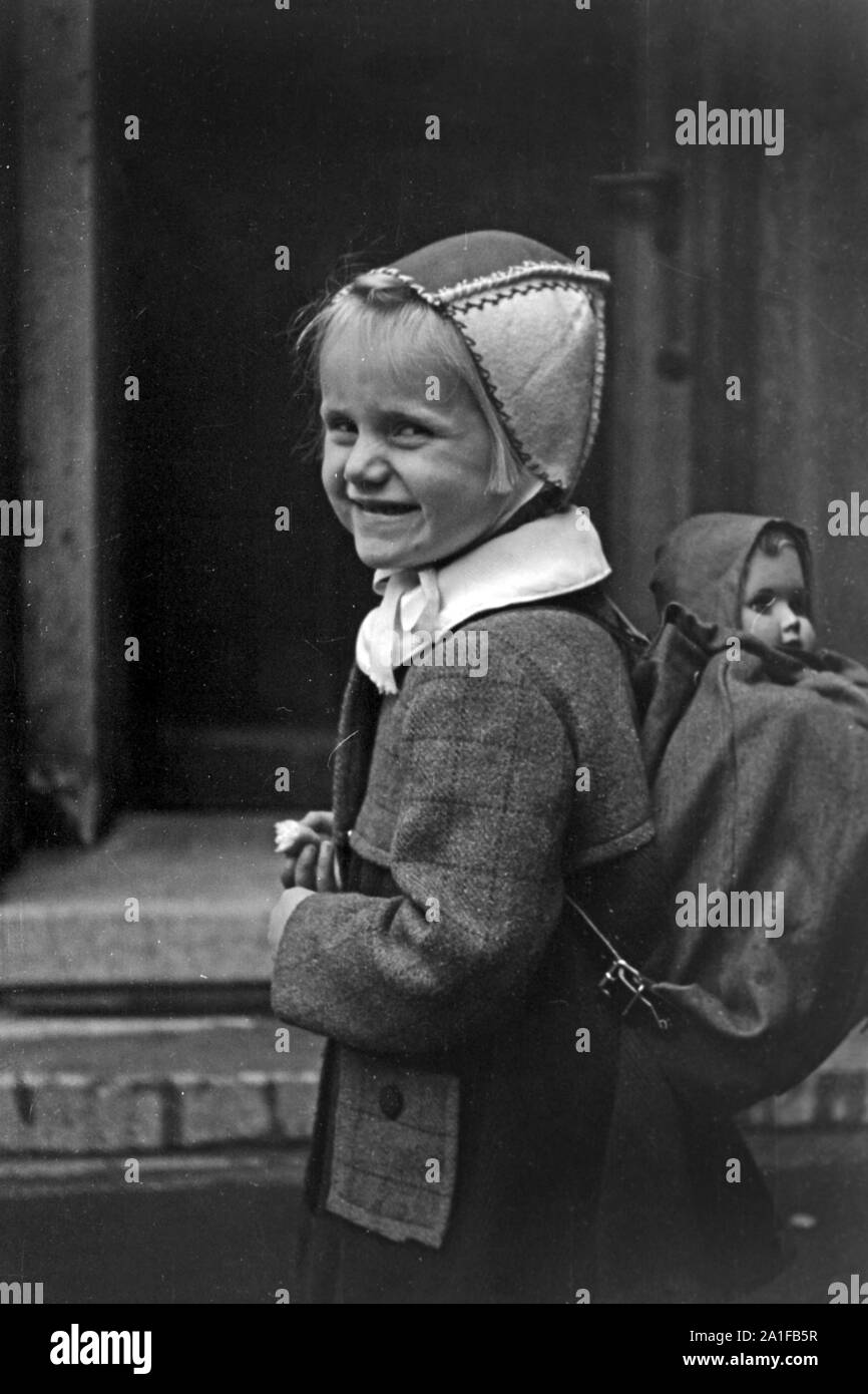 Mädchen mit ihrer Puppe im Gepäck auf dem Weg durch das verregnete Berlin, Deutschland 1949. Little girl with her dolls in a backpack on her way throuhgh the rainy Berlin, Germany 1949. Stock Photo