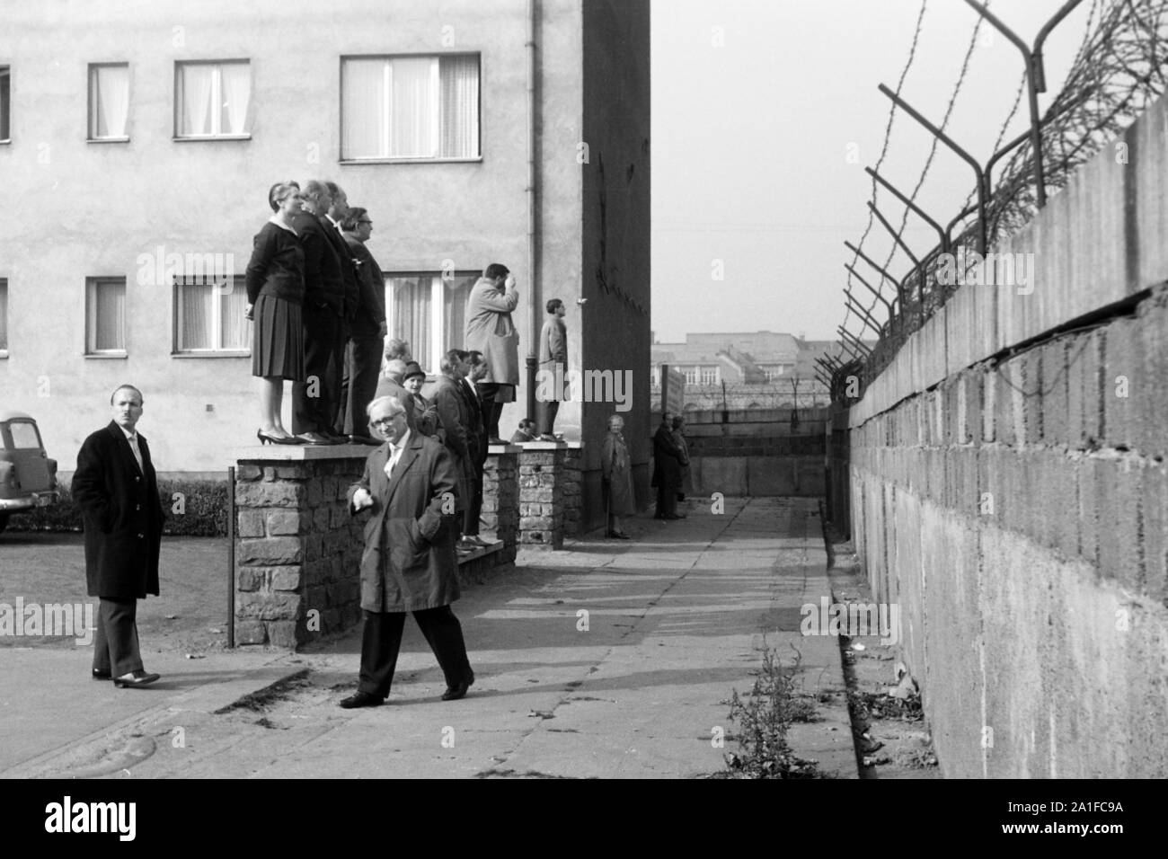Eine Reisegruppe schaut von einer Vorgartenmauer über die Mauer hinweg vom Westteil in den Ostteil von Berlin, Deutschland 1962. A tourist group standing on a small garden wall and watching from the West to the East over the Berlin wall, Germany 1962. Stock Photo