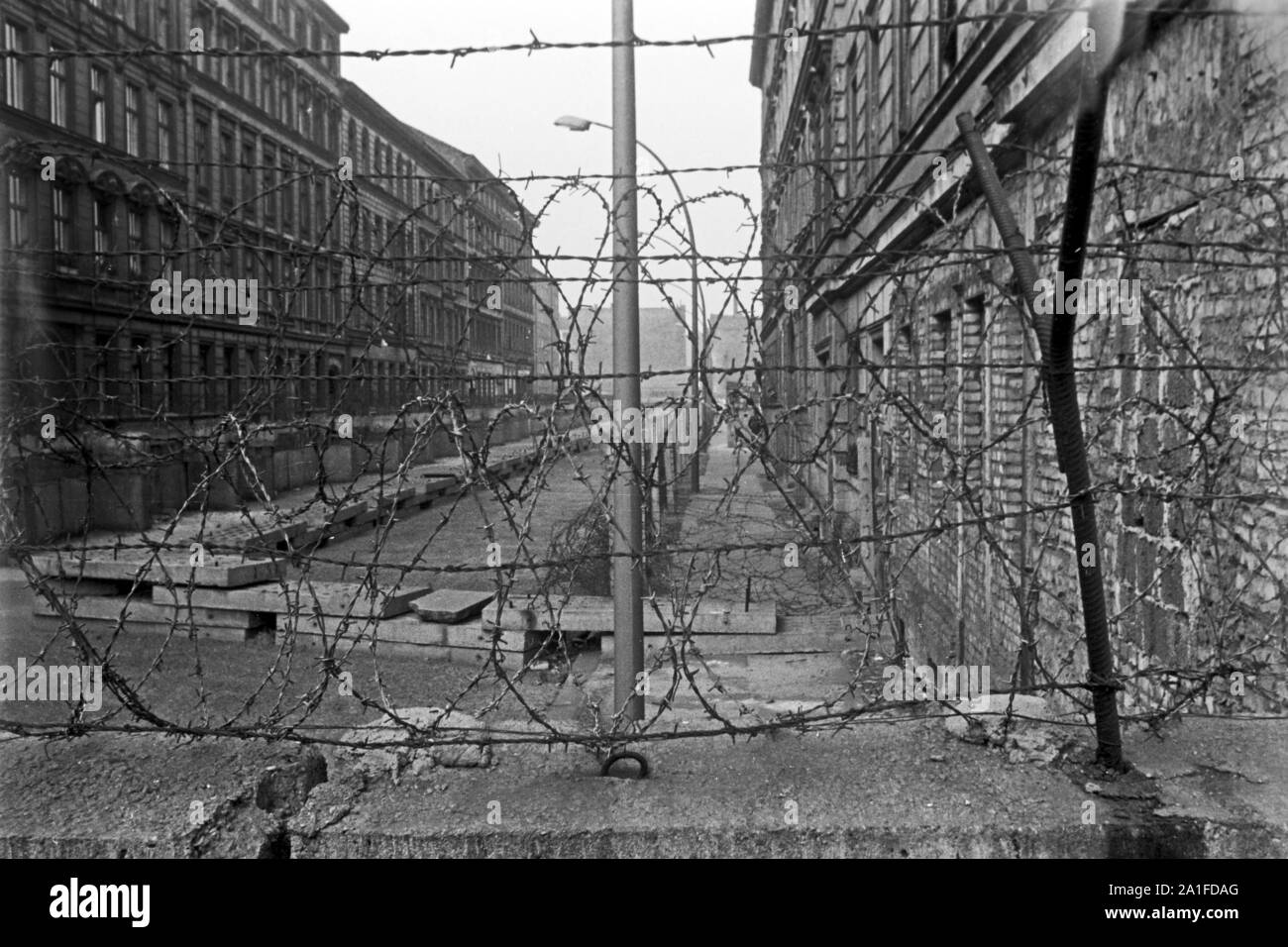 Blick durch Stacheldraht auf der Mauer in eine Straße im Ostteil der Stadt, Deutschland 1962. View through barbed wire on the Berlin wall to a street in the Eastern part of the city, Germany 1962. Stock Photo