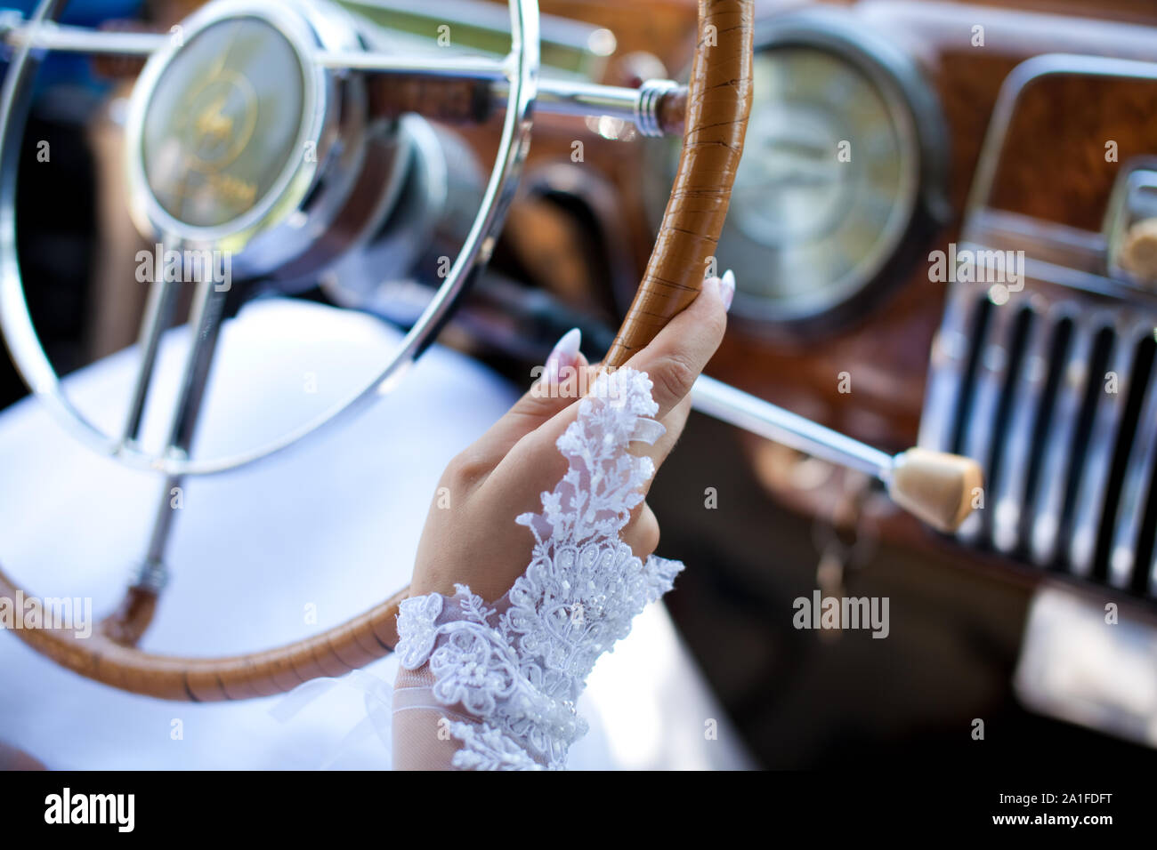 The brides hand is on the steering wheel of a retro car. Stock Photo
