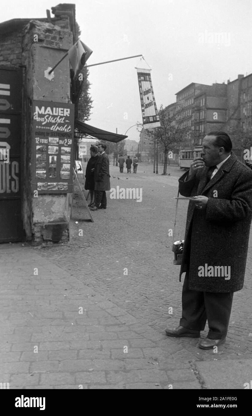 Ein Mann isst eine Wurst an einem Souvenirladen in Berlin, Deutschland 1962. Man snacking a sausage beside a souvenir shop at Berlin, Germany 1962. Stock Photo
