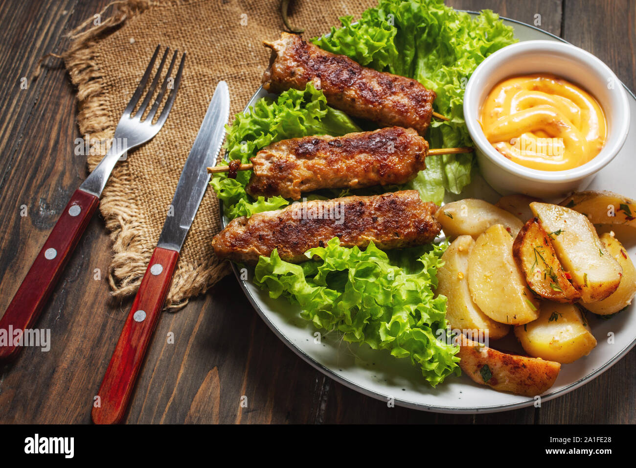 Grilled shish kebab served with fried potatoes and sauce on wooden