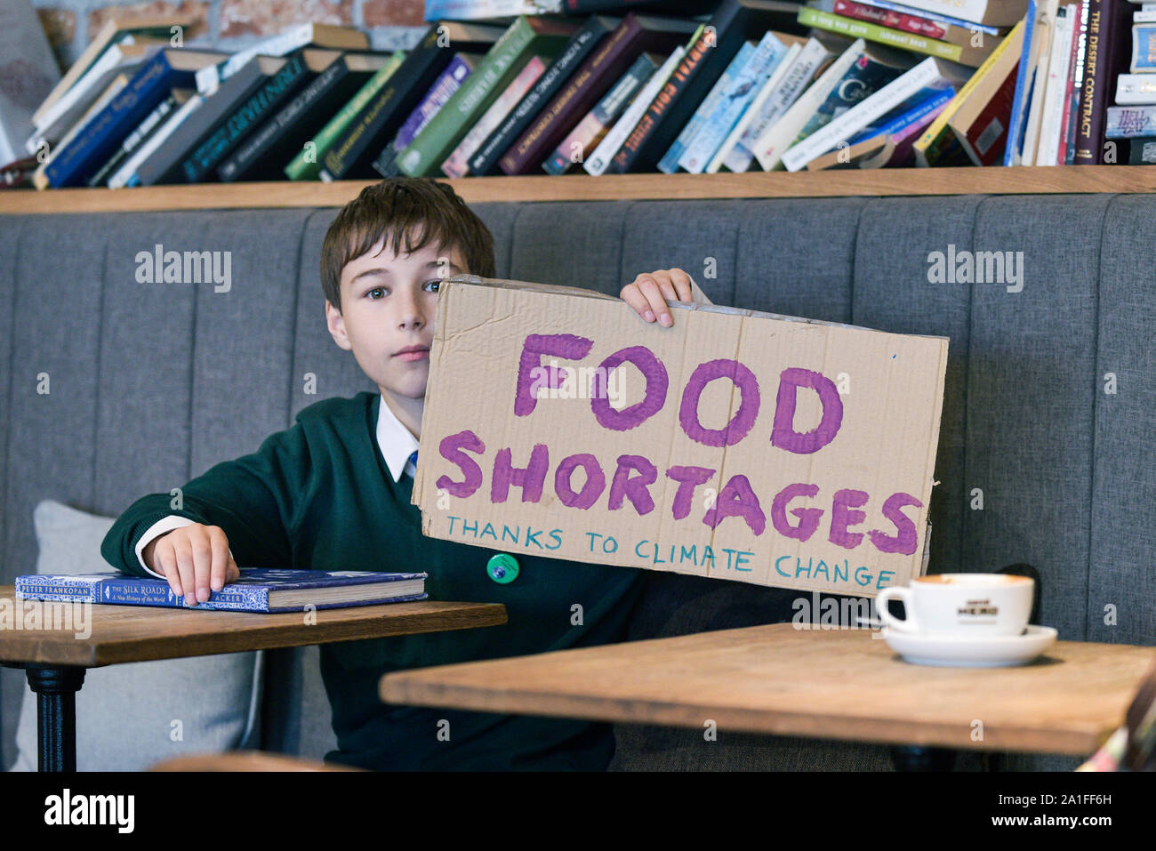A young school boy sitting in a coffee bar holding a hand written sign about food shortages. Stock Photo