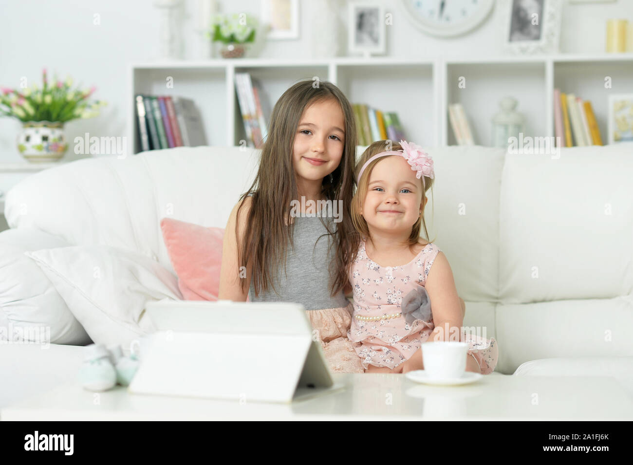 two cute little girls sitting on sofa and posing at home Stock Photo ...