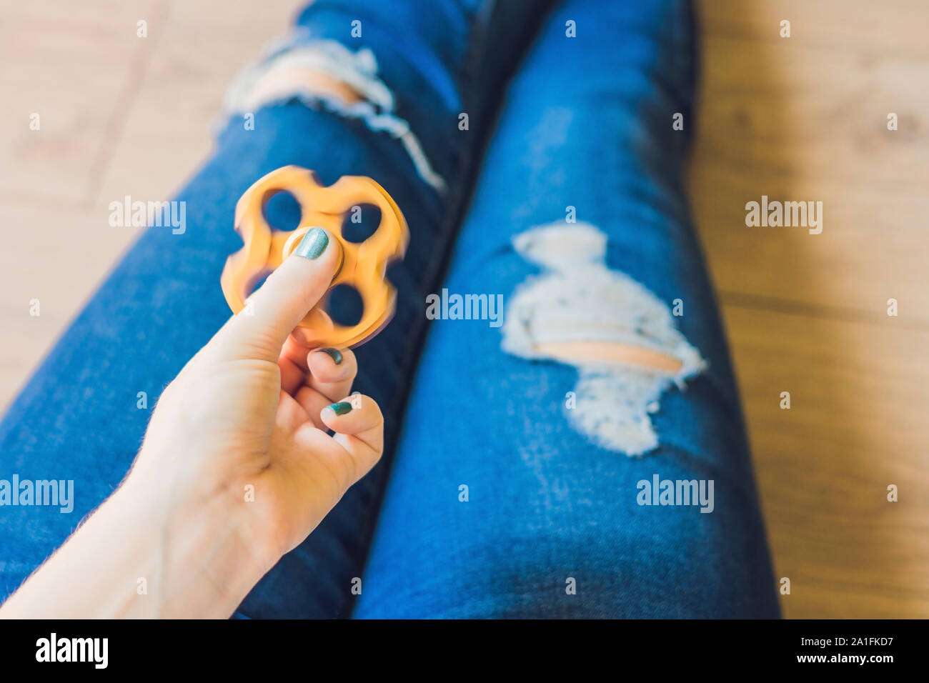 Girl teenager in holey jeans holds in hands and plays with spinner. Stock Photo