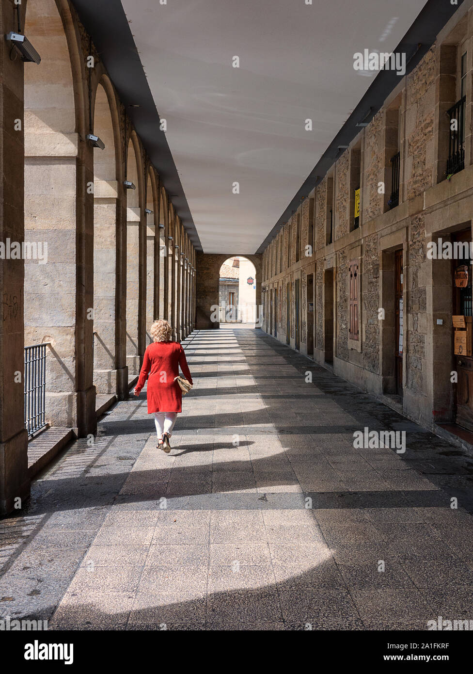 Woman in a red coat walking along the Los Arquillos passage in the Old Town of Vitoria-Gasteiz, Basque Country, Spain Stock Photo