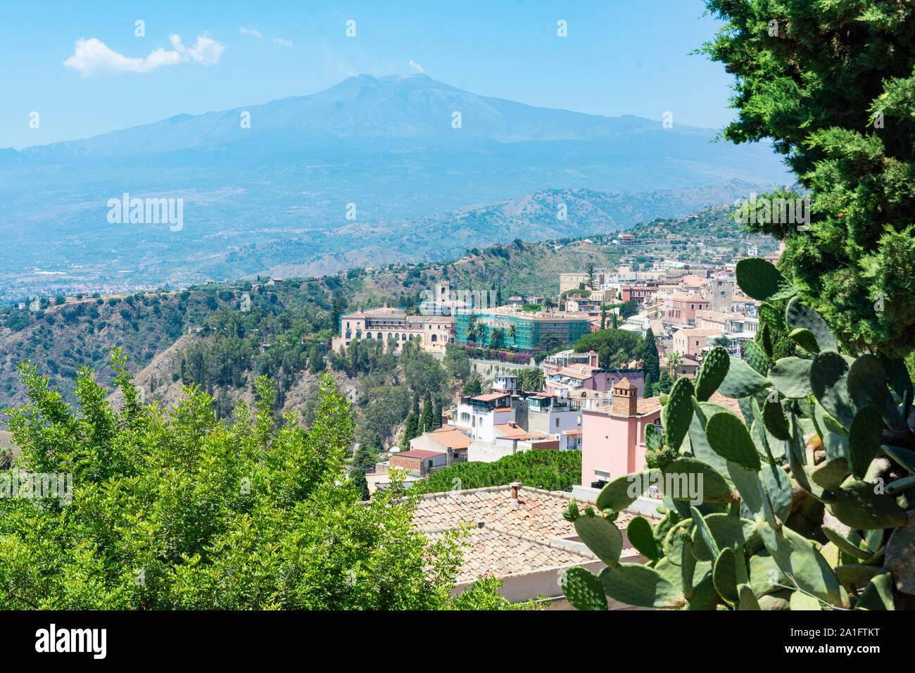 Beautiful view to Taormina city, Sicily, Italy and Etna volcano. Old houses and green plants. Smoke coming out of the crater of the volcano. Stock Photo