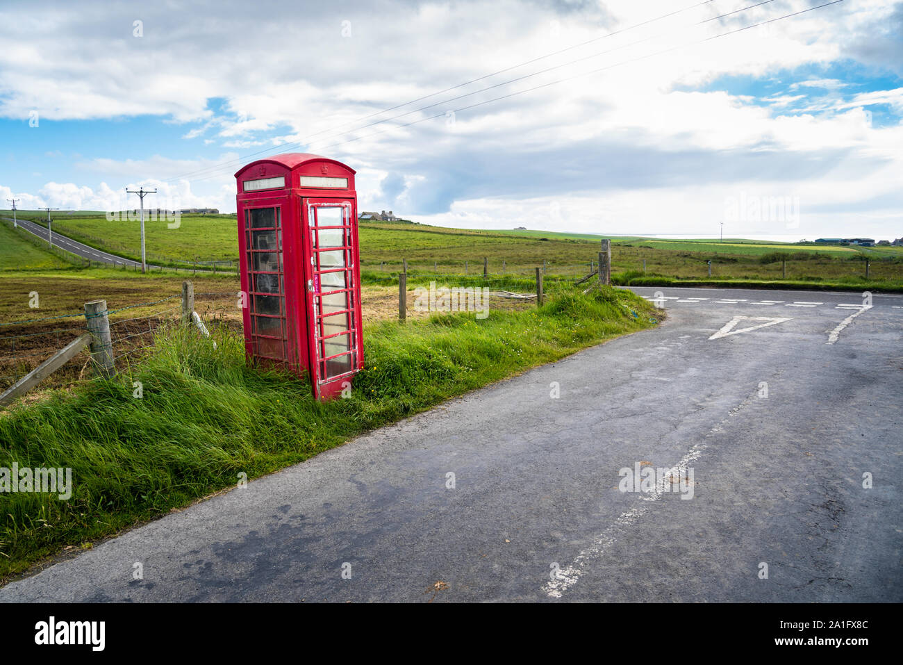 Lonely traditional British telephone booth near an intersection in the countryside on a partly cloudy spring day Stock Photo
