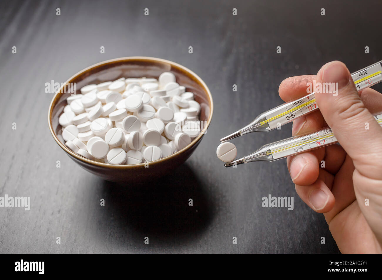 man is going to eat the drug tablets in bowl and holds two medical thermometer like chopsticks Stock Photo