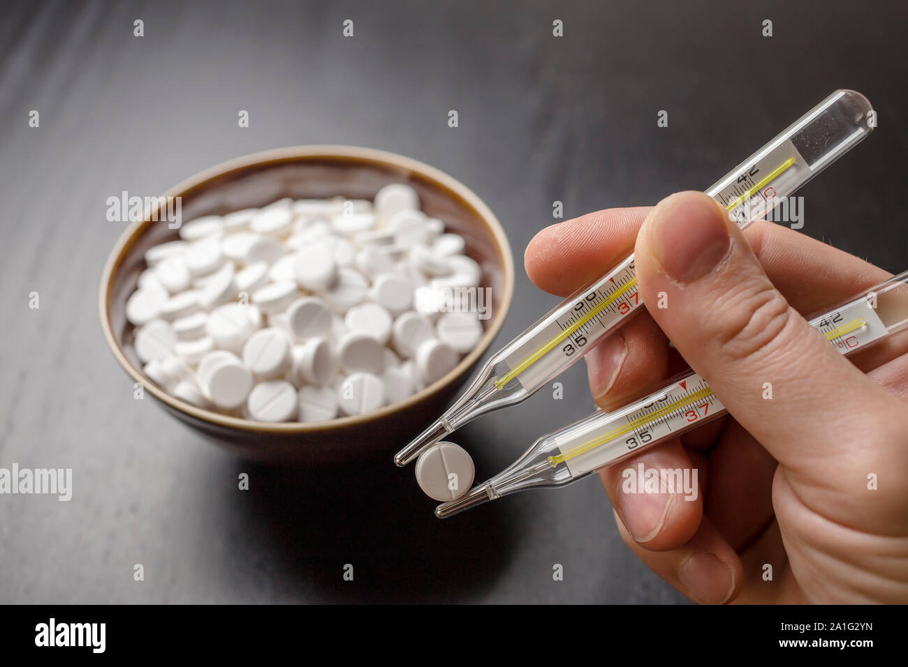 man is going to eat the drug tablets in bowl and holds two medical thermometer like chopsticks Stock Photo