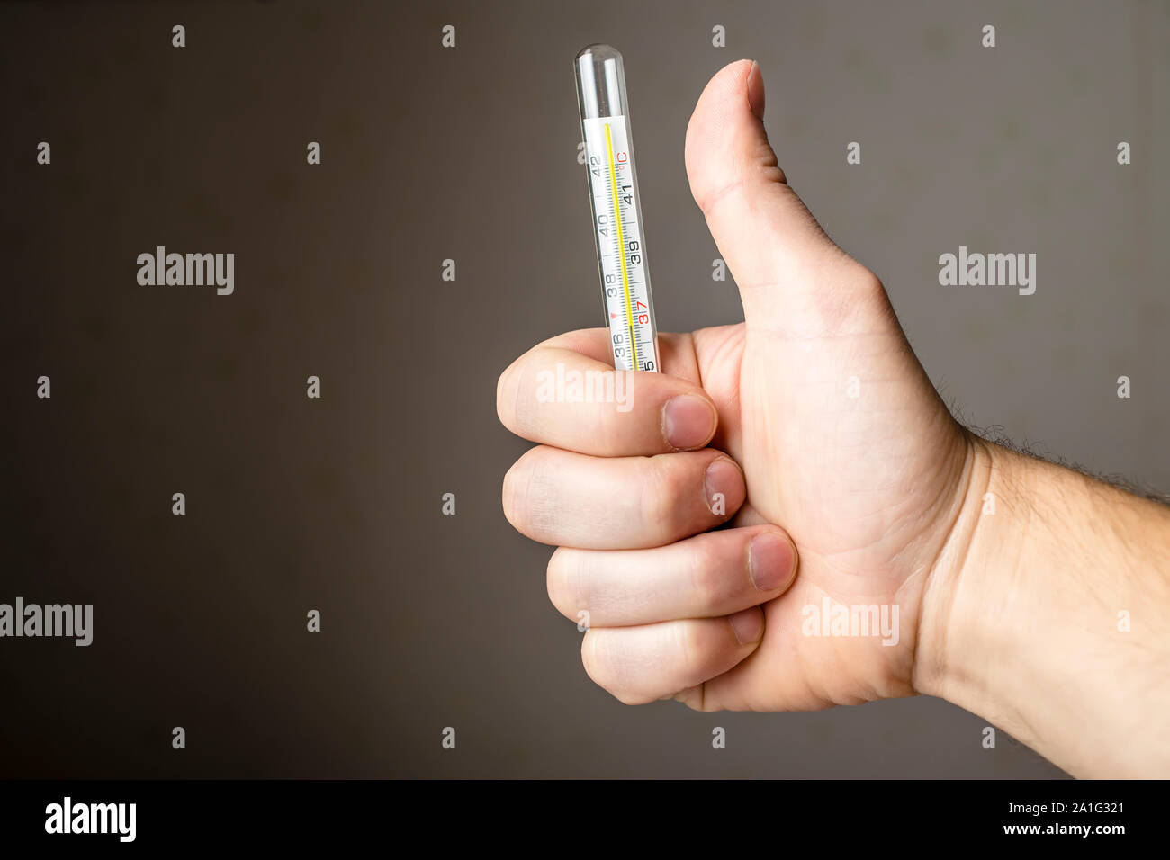 a sick man holding a medical thermometer and showing thumb indicating that he is all right Stock Photo
