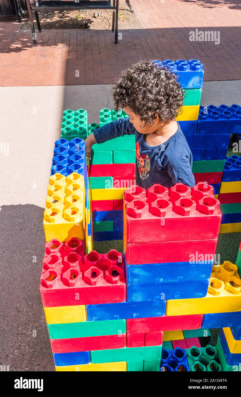 A 3-4 year old boy plays with large, colorful,  plastic building blocks outside at an outdoor mall in Santa Barbara, California. Stock Photo
