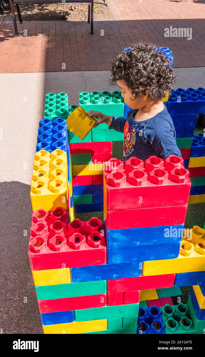 A 3-4 year old boy plays with large, colorful,  plastic building blocks outside at an outdoor mall in Santa Barbara, California. Stock Photo