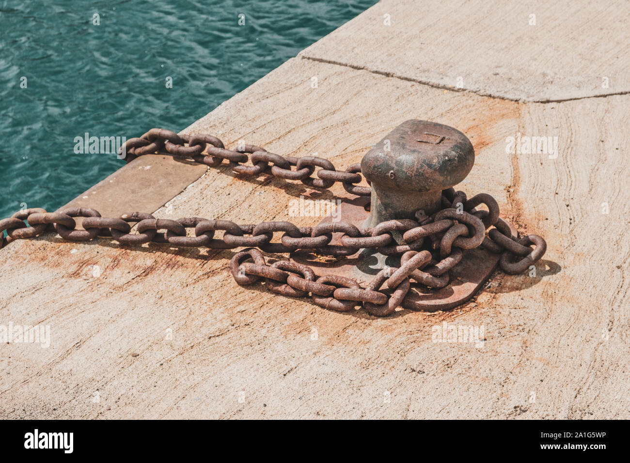 rusty chain on mooring bollard on dock closeup - ship anchored on harbor Stock Photo