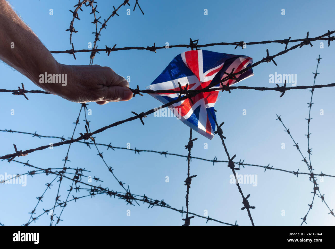 Hand and UK Union Jack flag on barbed wire fence. Brexit, asylum, immigration,border control... concept. Stock Photo