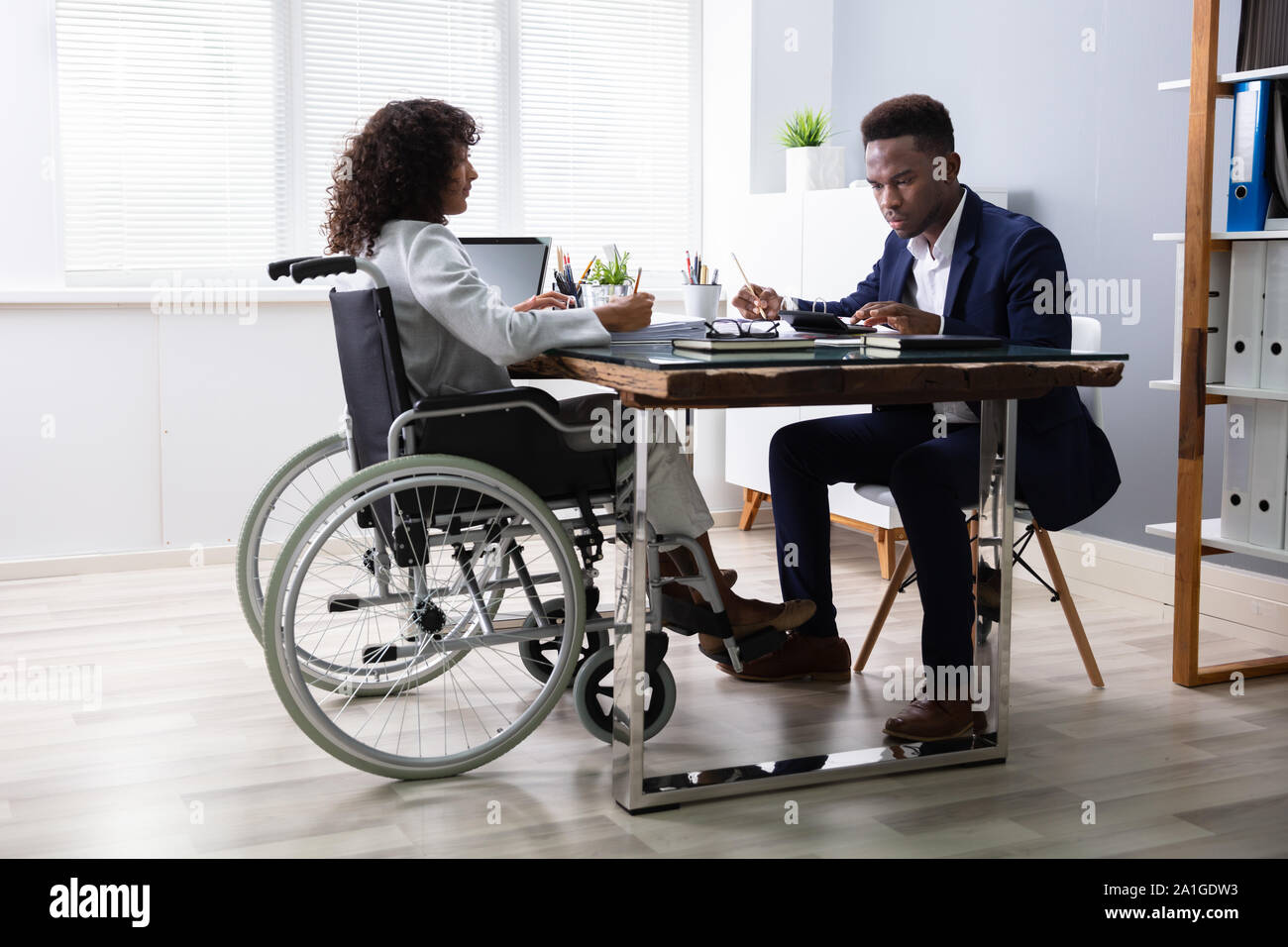 Businesswoman Sitting In Wheelchair Working In Office Stock Photo