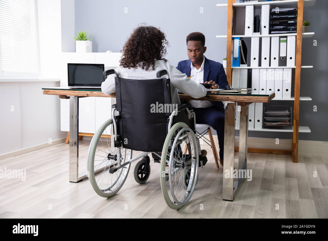 Businesswoman Sitting In Wheelchair Working In Office Stock Photo