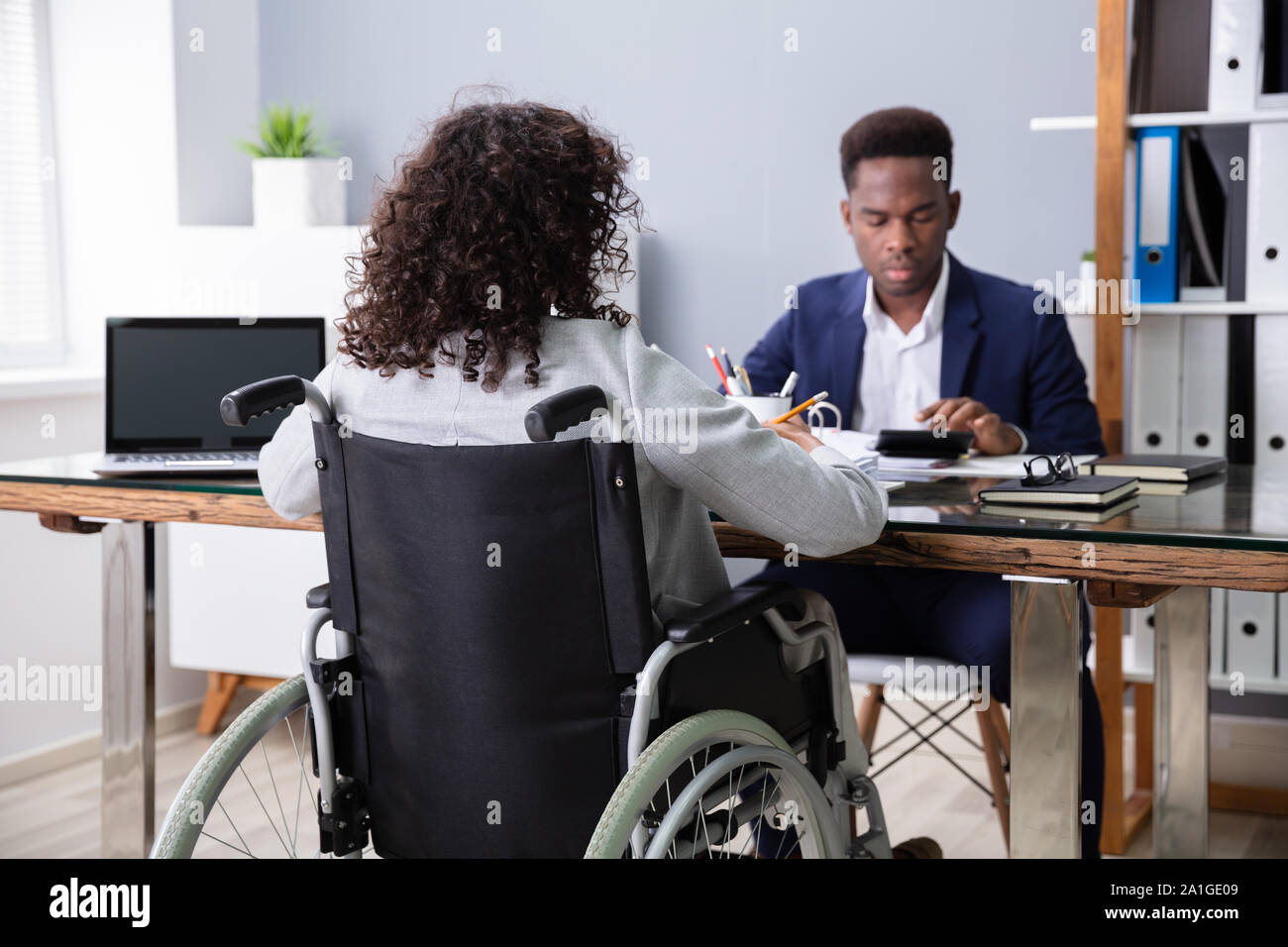 Businesswoman Sitting In Wheelchair Working In Office Stock Photo