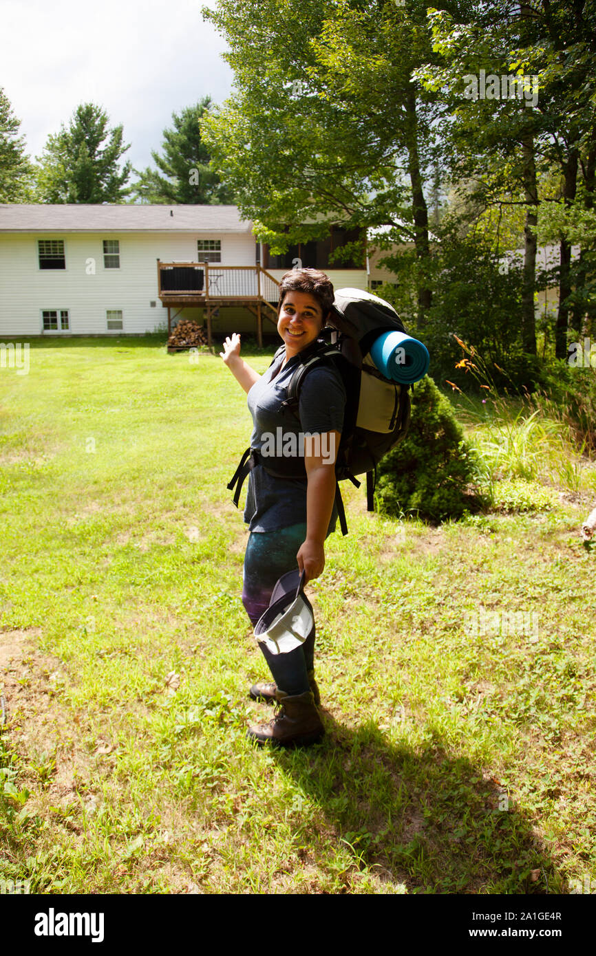 woman with a backpack and camp roll heading away from her house into the woods for adventure Stock Photo