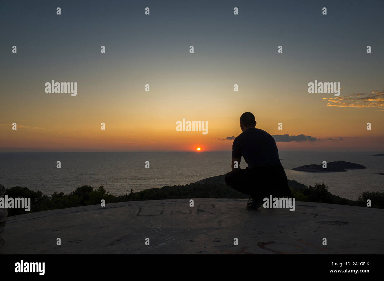 Beautiful nature and landscape photo of sunset at Adriatic Sea in Croatia. Nice calm summer evening. Man sitting watching sun. Happy and peaceful imag Stock Photo