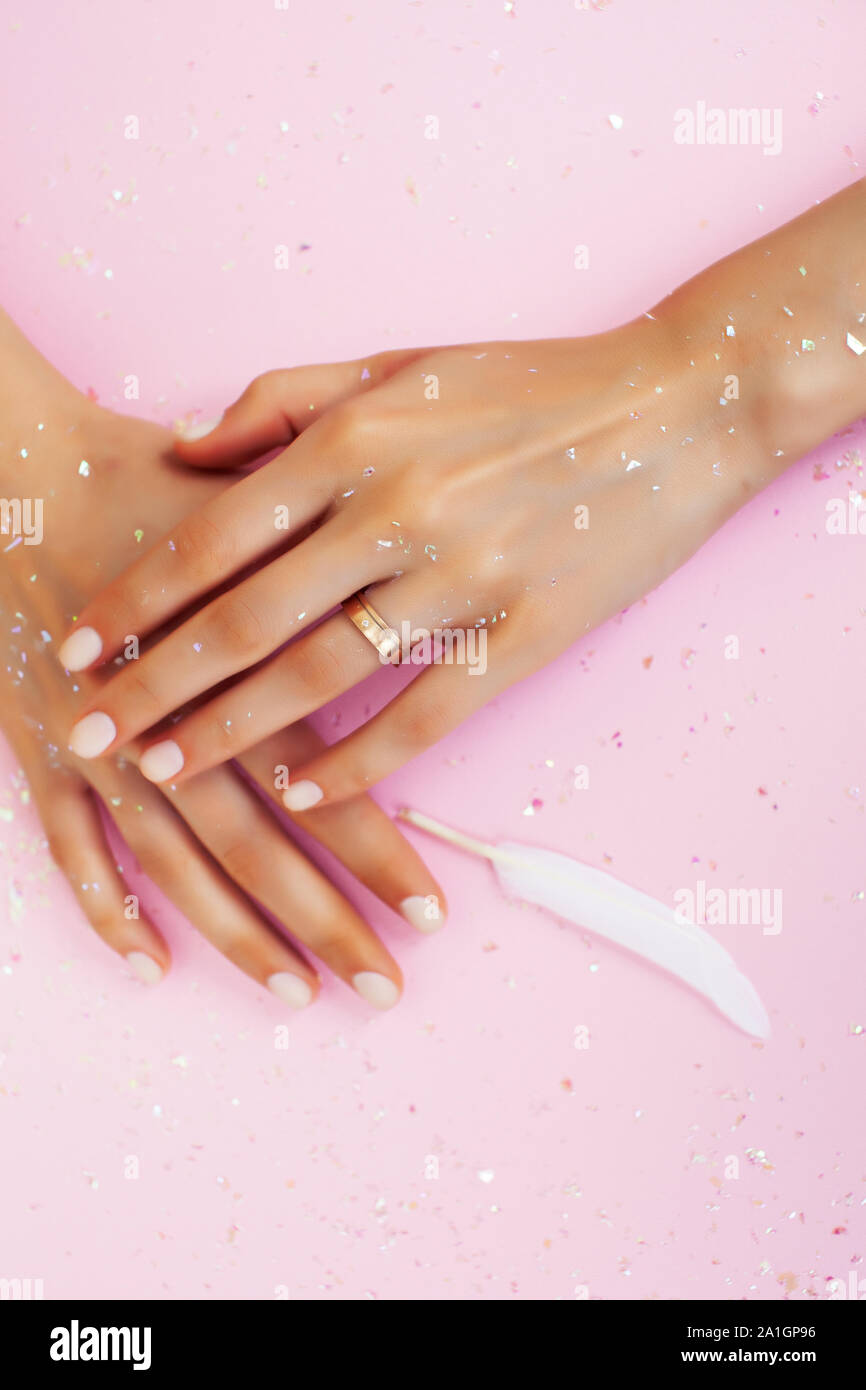 beautiful manicured woman hands with white feather on pink background, wearing wedding ring Stock Photo