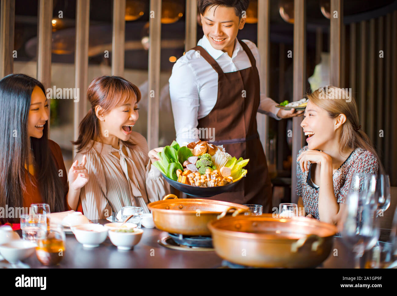 waiter  bring  vegetables for hot pot  and serving group of friends in restaurant Stock Photo