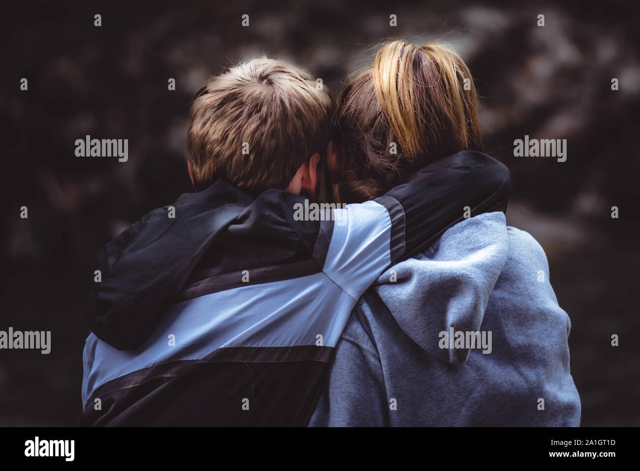 The close up of the backs of the teenage girl and boy hugging outside in the nature. Stock Photo
