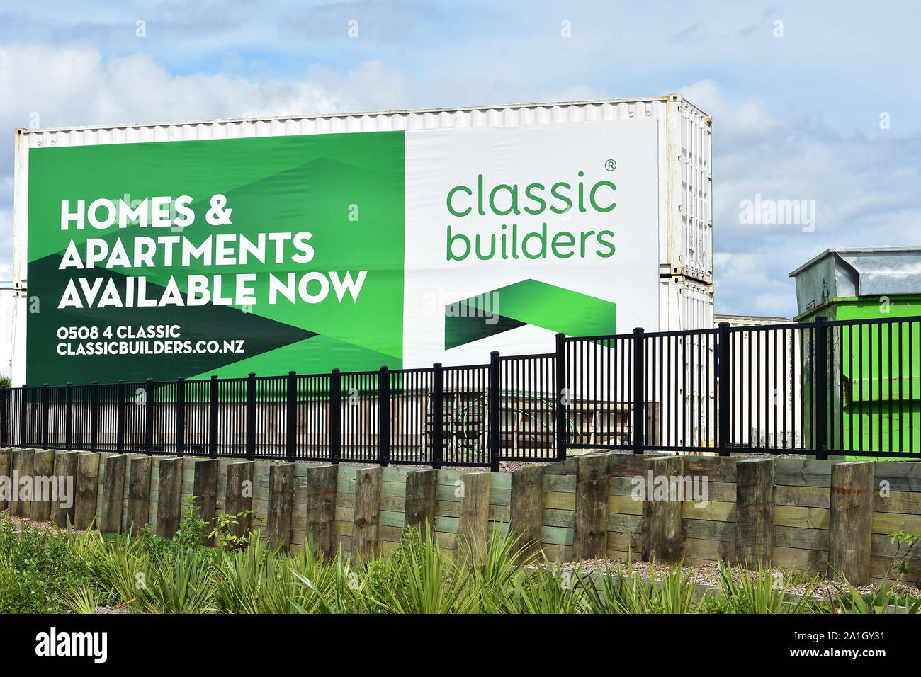 Shipping containers with large advertisement areas behind retaining wall with metal fence. Stock Photo