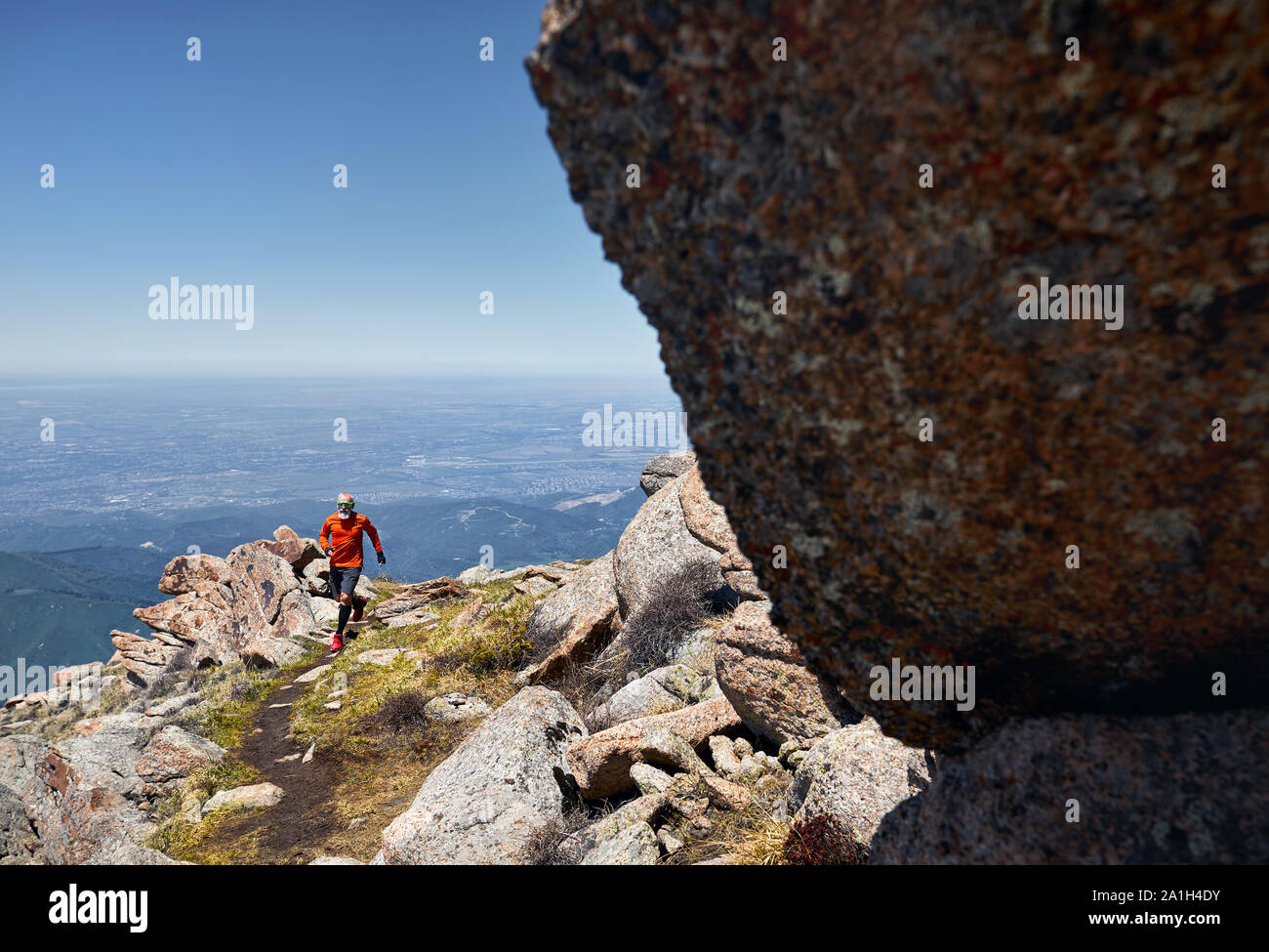 Runner athlete with beard in orange shirt running on the trail high in the mountains Stock Photo