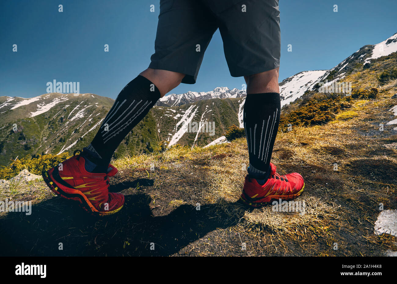 Close up of hiker legs in red shoes are climbing in the mountains at blue sky background. Healthy lifestyle. Outdoor travel concept. Stock Photo