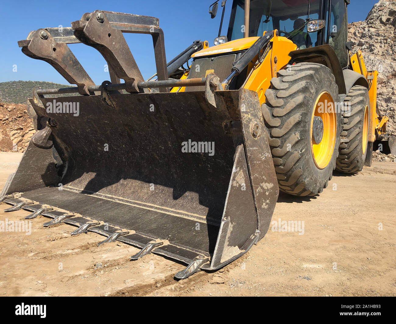 Bucket of yellow loader backhoe digging a trench during road