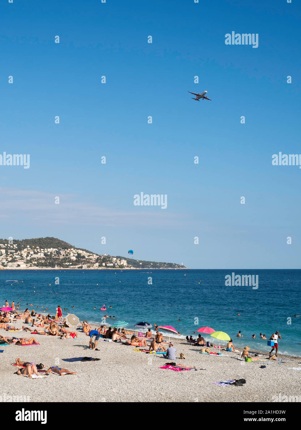 People sunbathing on the beach as a plane flies over to land in Nice, France, Europe Stock Photo