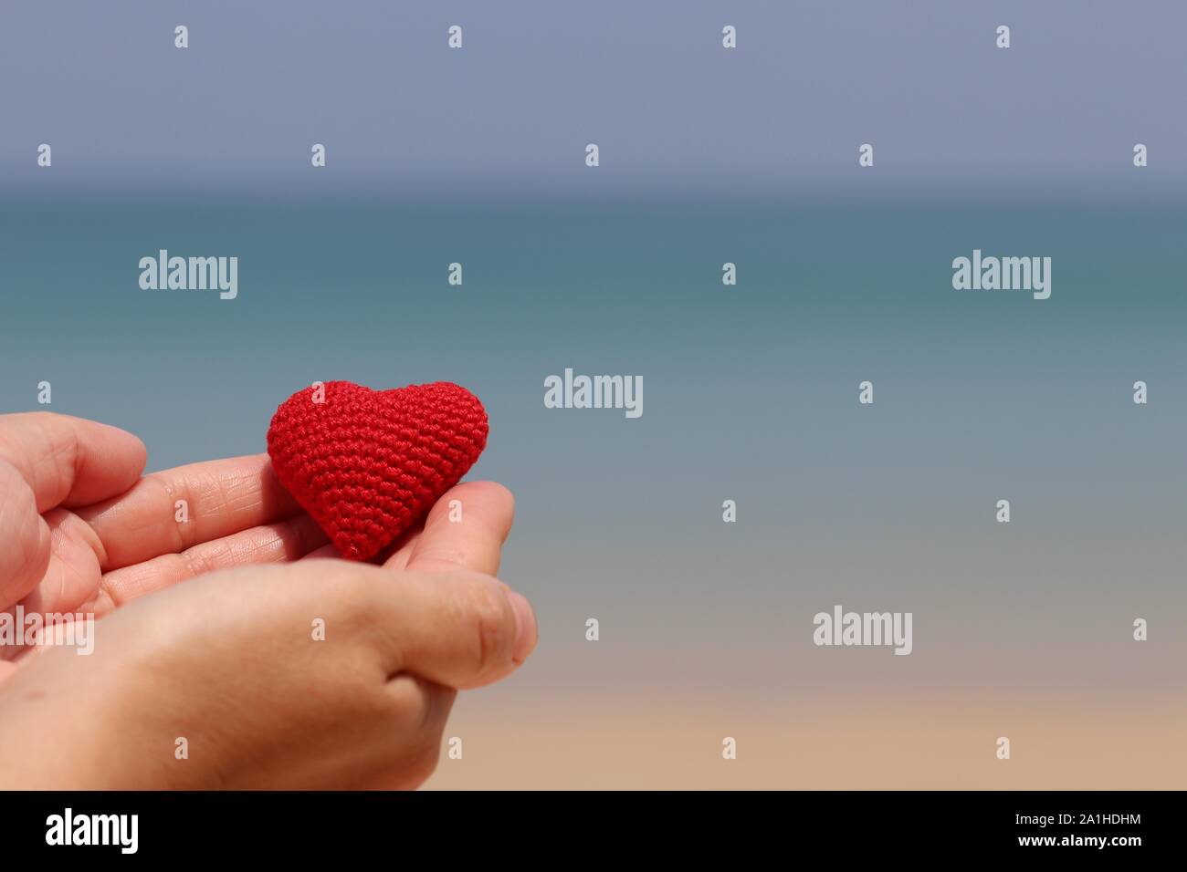 Love on the beach, red knitted heart in a female hands against the blue sea. Concept of a romantic holidays and honeymoon Stock Photo