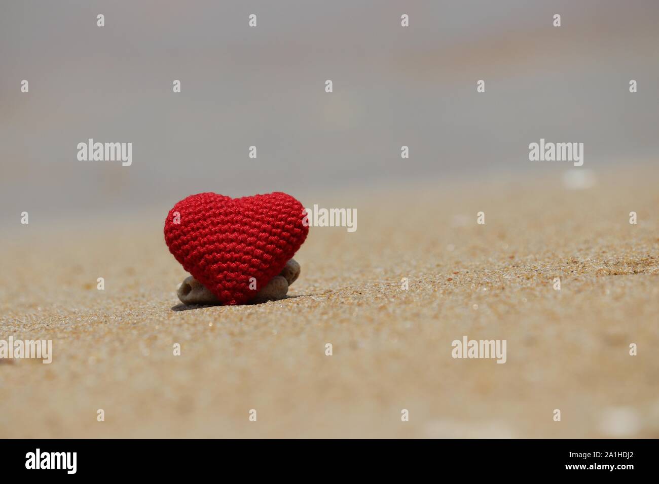 Romantic holidays, red knitted heart on a sand of a sunny beach. Concept of love, vacation and romance Stock Photo