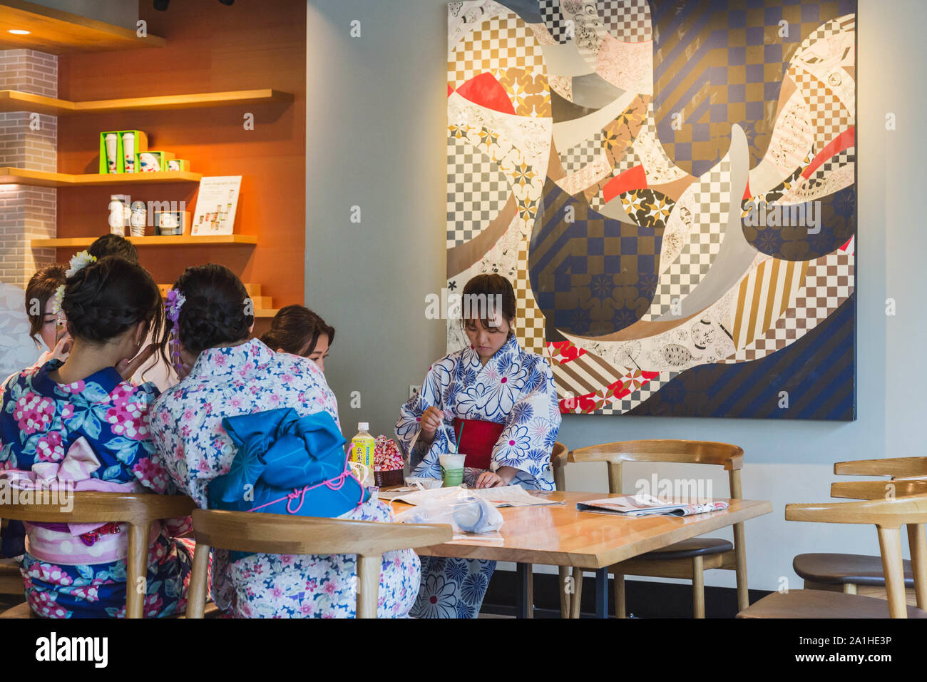 Young Japanese women in summer kimono relax with cold drinks in front of large printed wall art at Starbucks Coffee located in Asakusa, Tokyo, Japan. Stock Photo