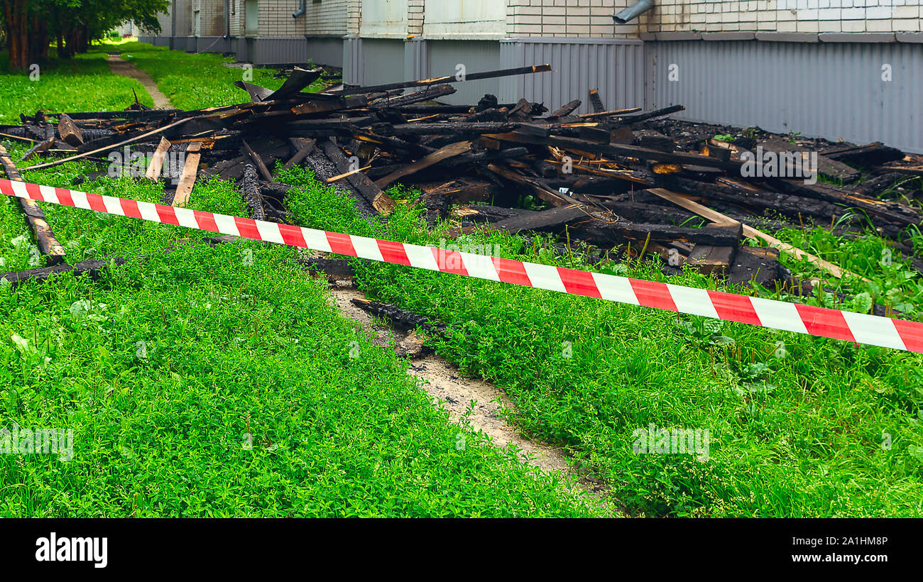 Red and White Safety Tape and Black Charred Rafters, Roof Framework on the Lawn near the Apartment Building after the Fire. Safety, Insurance Concept. Stock Photo