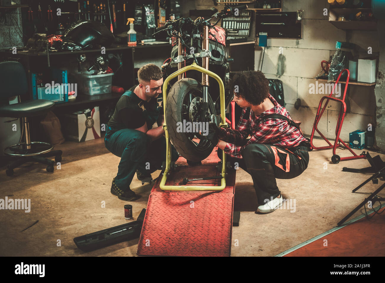 Mechanic and his helper repairing a motorcycle in a workshop Stock Photo