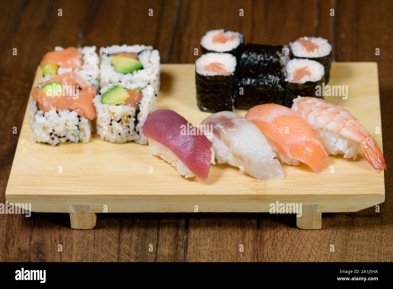 mix of sushi, sushi roll and nigiri with salmon, tuna, sea bass, shrimp, avocado served on a wooden plate, dark wood table background Stock Photo
