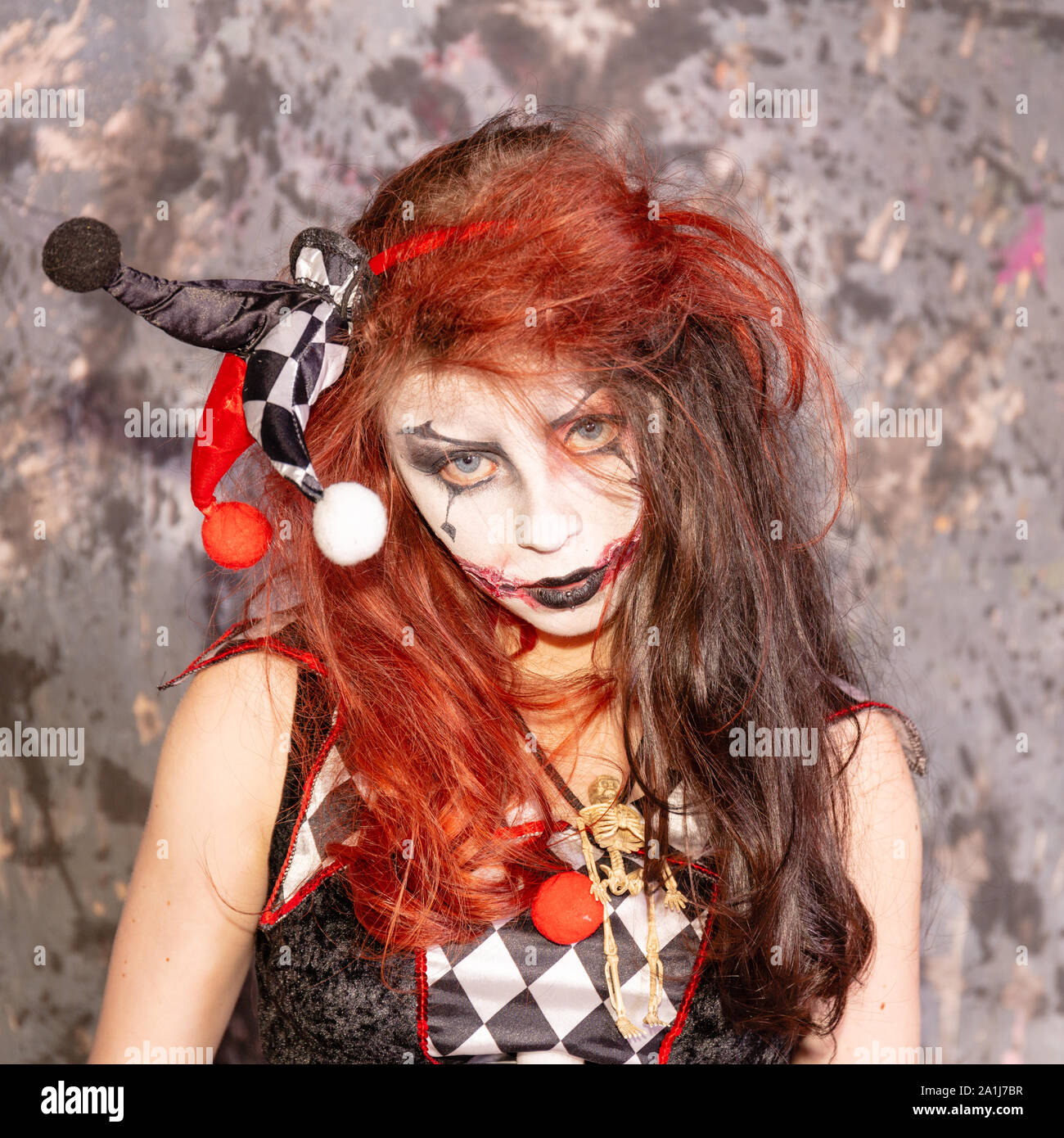 Young female in Harlequin costume smiles wickedly as blood oozes from her mouth Stock Photo