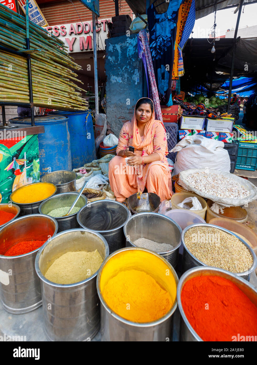 Street scene, Mahipalpur district, a suburb of New Delhi, capital city of India: roadside stall selling brightly coloured spices and female shopkeeper Stock Photo